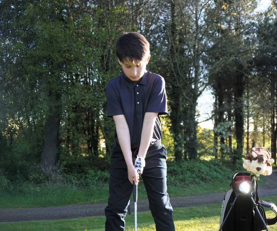A boy playing golf wearing ProQuip's Juniors golf clothing range