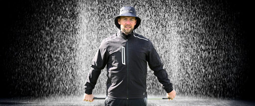 A man holding a golf club wearing a waterproof hat and jacket